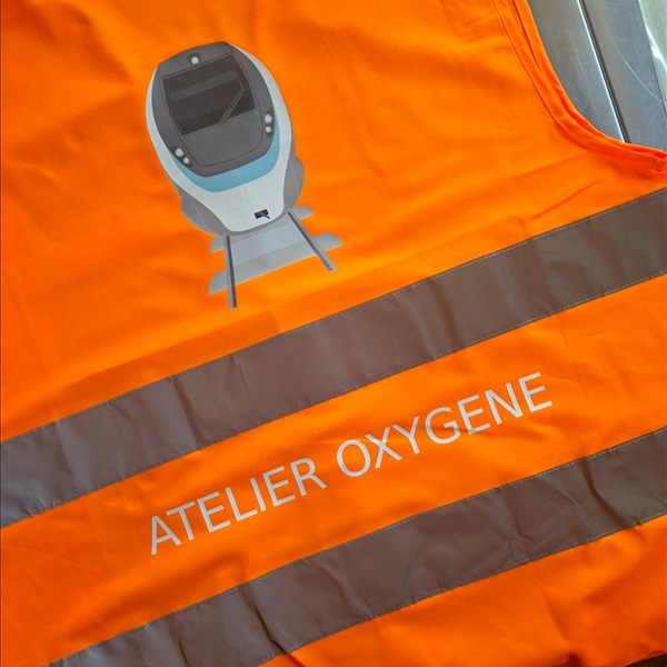 Gilet de sécurité orange 2 bandes Yoko HVW102 imprimé au dos d'une illustration de train et du texte Atelier Oxygène entre les bandes réfléchissantes